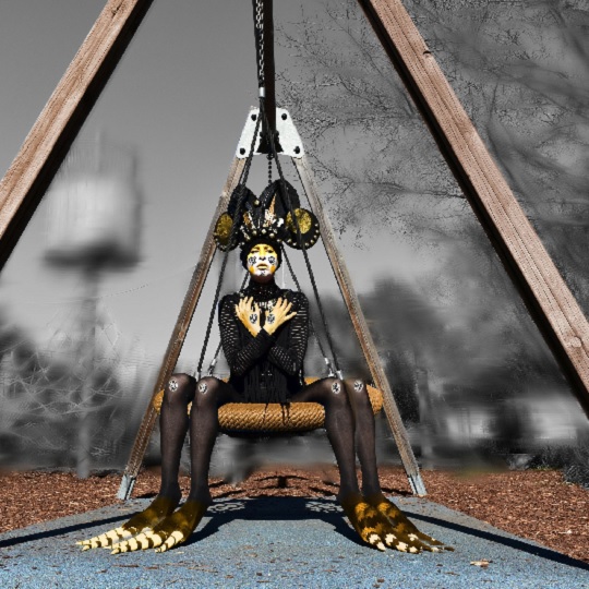 Woman dressed as spider-like creature with four legs in black and yellow costume and matching face paint, she wears a large back and gold  headdress , her arms make a letter x across her chest and she sits on park swing/web equipment